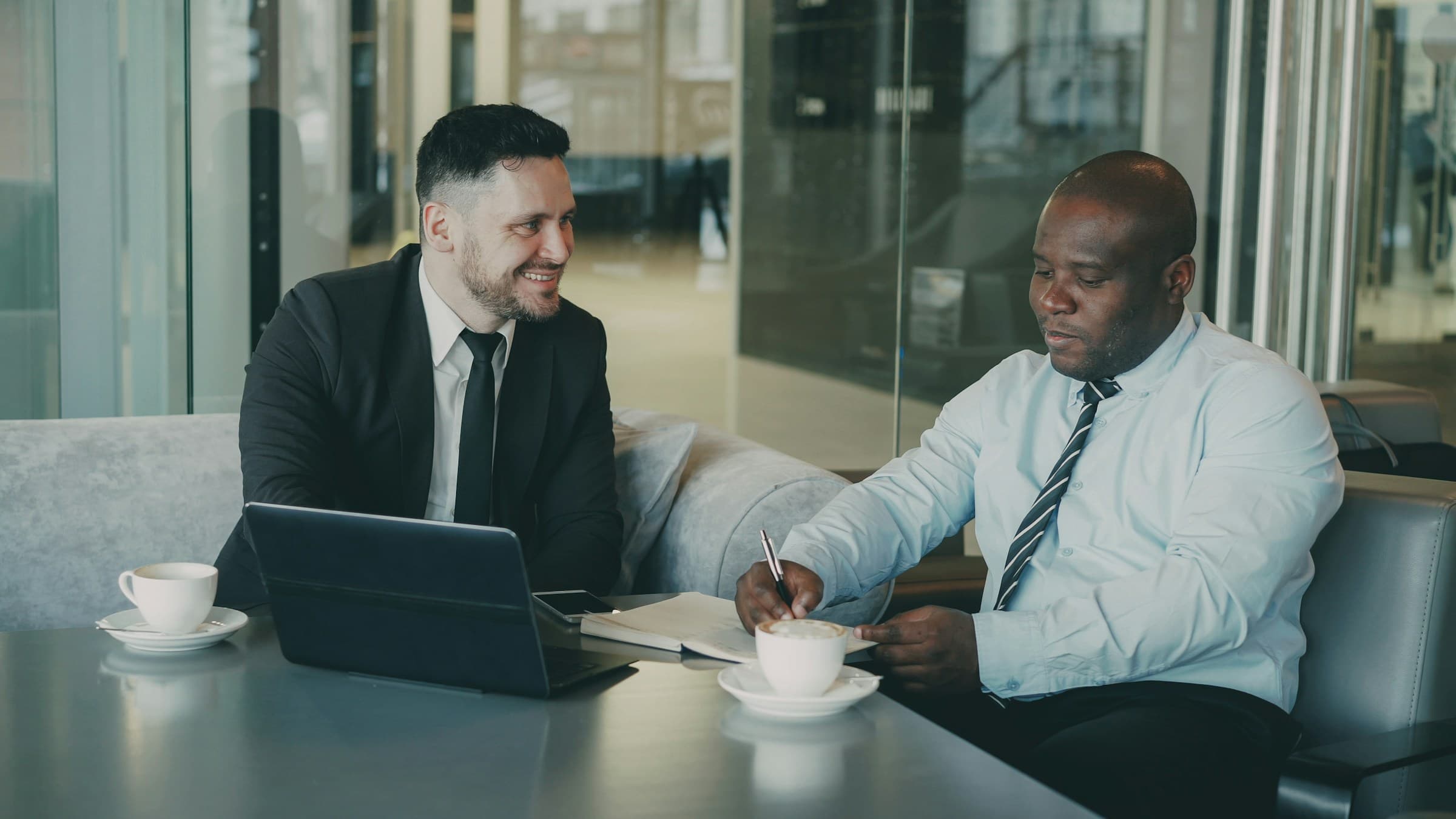 Two people in conversation at a table with a notebook between them.